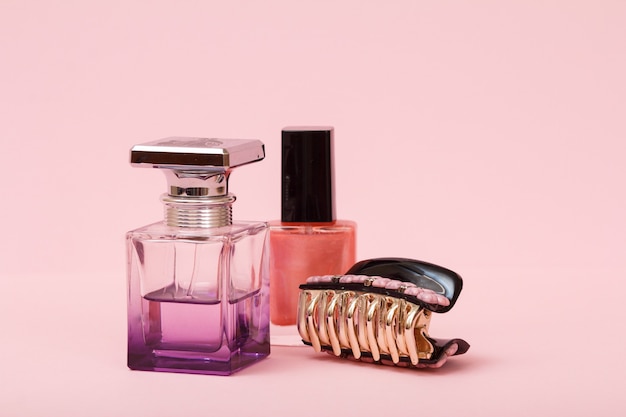 Perfume de mulher, frasco com esmalte e prendedor de cabelo em um fundo rosa. Cosméticos e perfumes femininos.