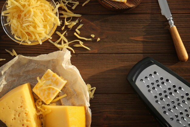 Pergamino con diferentes tipos de queso y rallador sobre mesa de madera