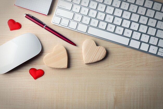 Periféricos de computadora con bolígrafo de corazones y cuaderno en mesa de madera clara