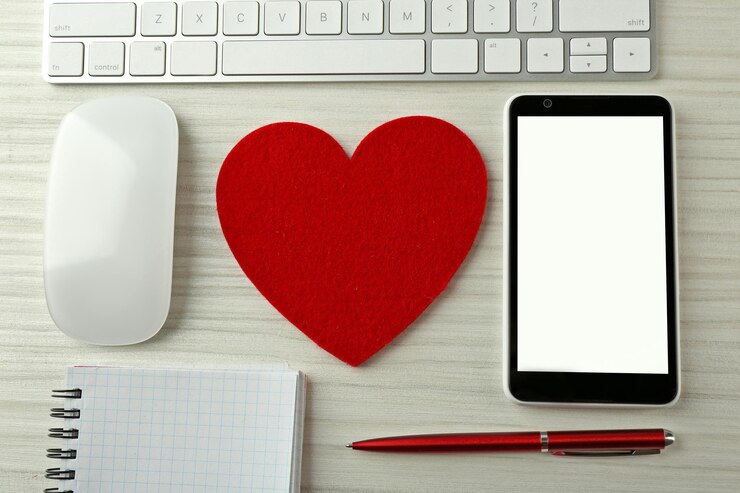 Foto periféricos de computadora con cuaderno de corazón rojo y teléfono móvil en mesa de madera clara