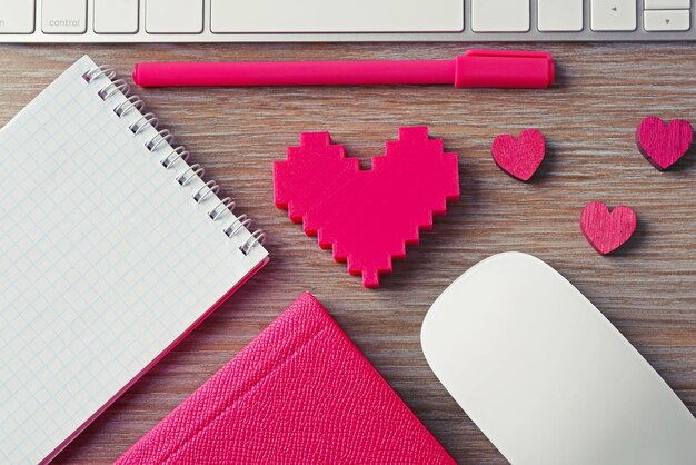 Periféricos de computador com caneta de corações rosa e notebooks na mesa de madeira