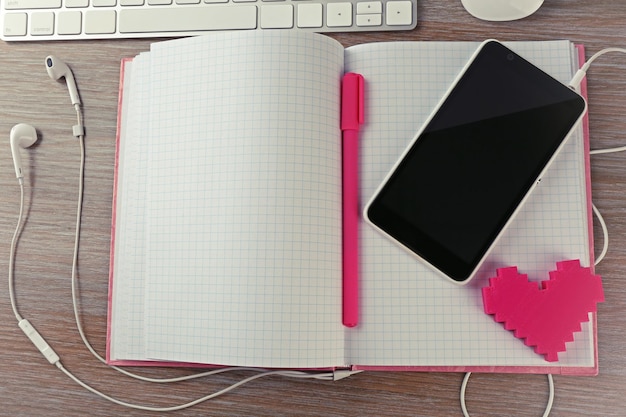 Periféricos de computador com notebook de coração rosa e celular na mesa de madeira