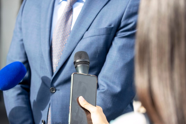 Foto periodista en una conferencia de prensa con micrófono y teléfono inteligente haciendo una entrevista con los medios