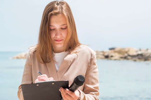 Periodista femenina de pie junto al mar