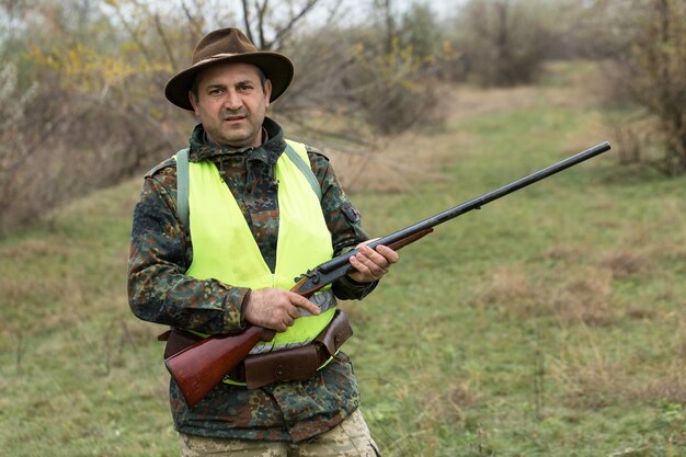 Período de caza temporada de otoño abierta Un cazador con un arma en las manos con ropa de caza en el bosque de otoño en busca de un trofeo Un hombre se para con armas y perros de caza rastreando el juego