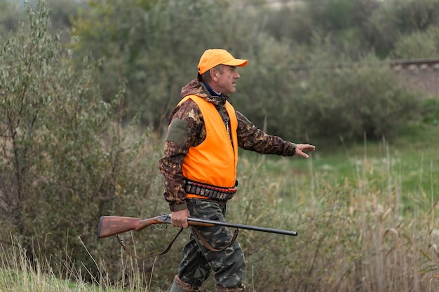 Periodo de caza, temporada de otoño abierta. Un cazador con una pistola en sus manos con ropa de caza en el bosque de otoño en busca de un trofeo. Un hombre está de pie con armas y perros de caza rastreando el juego.