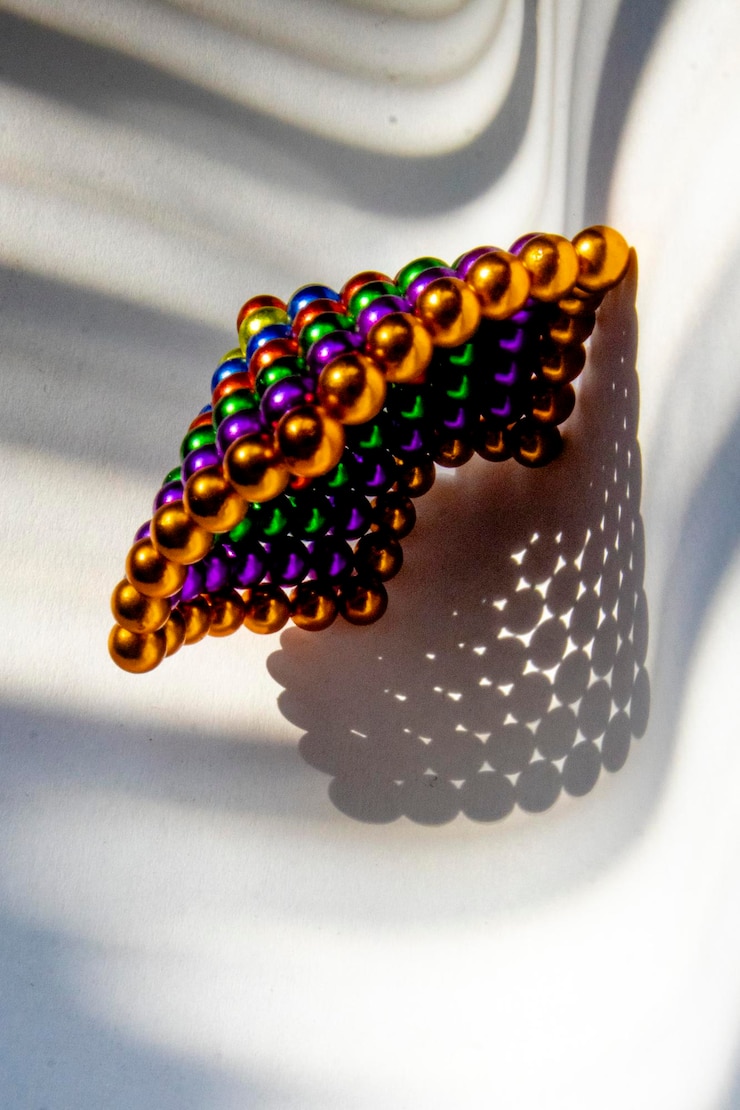 Foto perlas de colores con forma de pirámide en base blanca con iluminación de sombra a rayas