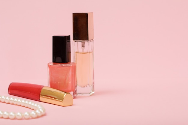 Perlas, lápiz labial, esmalte de uñas y perfume sobre un fondo rosa. Joyería, cosmética y complementos para mujer.