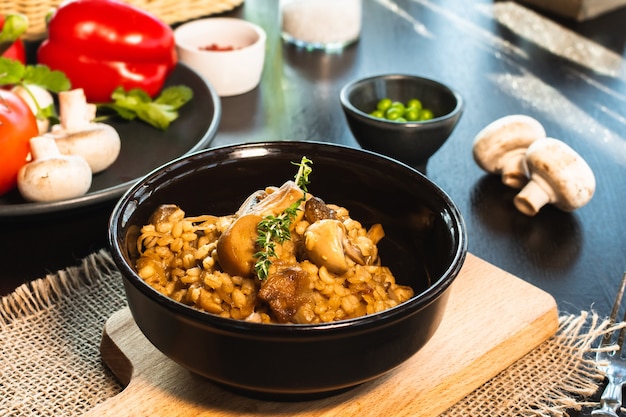 Perlgerste Risotto oder Orzotto mit Pilzen in dunkler Schüssel auf hölzernem Hintergrund. Selektiver Fokus.