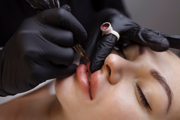 Permanent Make-up für nackte Lippen Der Kosmetiker im Salon führt ein Tätowierverfahren mit einer Tätowiermaschine in der Nähe durch