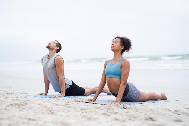 Permita que todos os seus sentidos sintam uma sensação de calma Foto de um jovem e uma mulher praticando ioga juntos na praia
