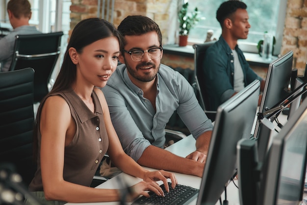 Foto permítanme explicarles a dos jóvenes positivos que miran el monitor de la computadora y hablan sobre el trabajo.