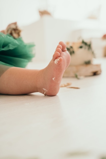 Perna de criança no fundo da celebração do bolo do primeiro ano da decoração infantil da criança ...