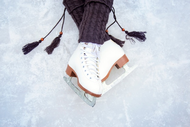 Pernas calçadas com patins brancos. bela pose das pernas na pista de gelo. polainas de malha quente com borlas e patins artísticos clássicos