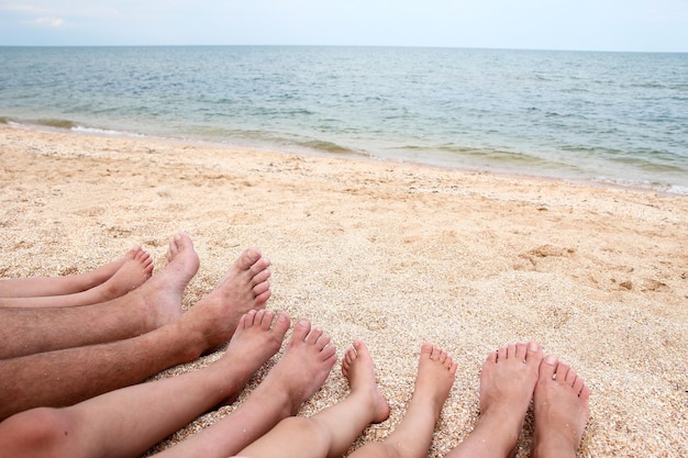 Pernas da linda família inteira na areia perto do fundo do mar