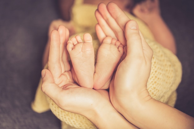 Pernas de bebê recém-nascido pequeno na mão linda de mães com foco suave nos pés do babie