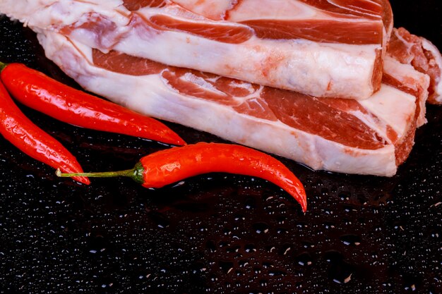 Pernas de cordeiro cru com pimenta na bandeja de pedra na mesa, foco seletivo