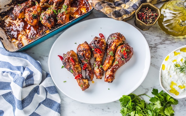 Pernas de frango assado e churrasco grelhado na chapa branca com decoração de ervas.