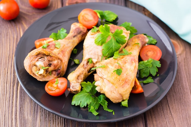 Pernas de frango assado em especiarias com tomates e verduras em um prato sobre uma mesa de madeira