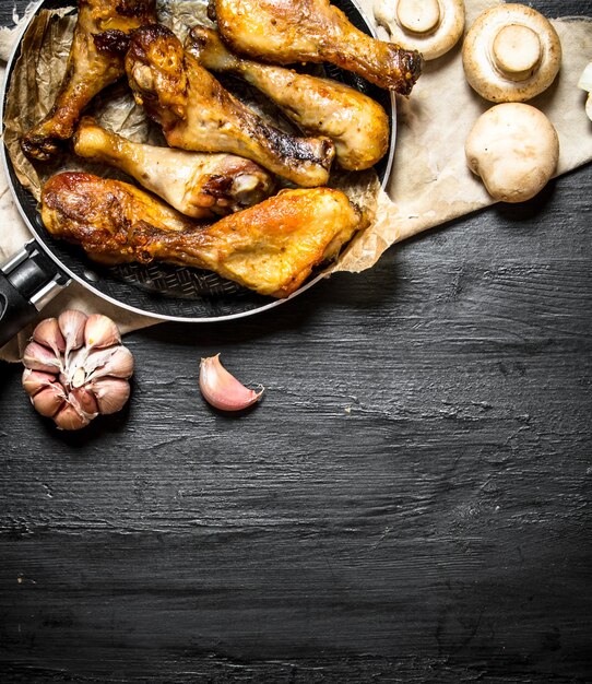 Pernas de frango com cogumelos e alho em um fundo preto de madeira