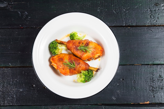 Foto pernas de frango com legumes na mesa de madeira.