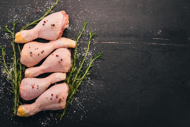 Pernas de frango cru com alecrim e especiarias em um fundo preto de madeira Vista superior Espaço livre para texto