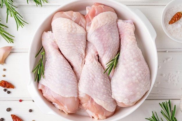 Pernas de frango cru cru em um prato branco sobre um fundo branco de madeira Vista superior