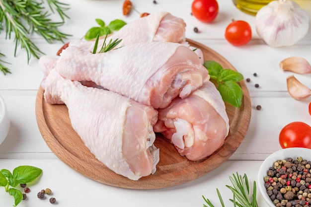 Pernas de frango cru cru em uma placa de corte em um fundo branco carne com ingredientes para cozinhar