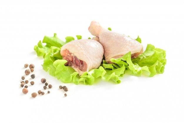 Pernas de frango cru e salada verde, isoladas no fundo branco.