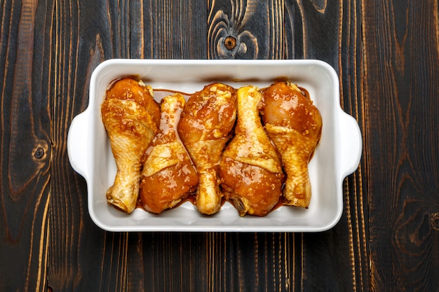 Pernas de frango cru em assadeira em uma mesa de madeira