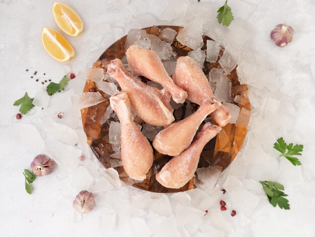 Pernas de frango cru no gelo com limões e pimenta vermelha em cima da mesa