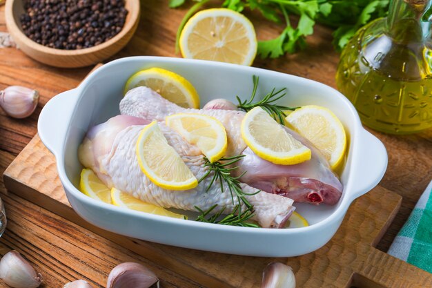 Pernas de frango crua sem coca, baquetas na tábua de madeira, carne com ingredientes para cozinhar