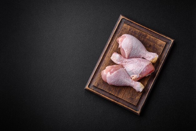 Pernas de frango cruas com especiarias e ervas salgadas em um fundo de concreto escuro