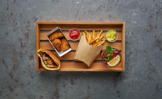 Pernas de frango frito crocante com batatas fritas e limonada na bandeja de madeira. Conceito de comida de rua, composição horizontal com espaço de cópia