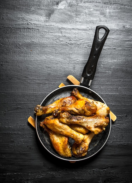 Pernas de frango frito em uma frigideira em um fundo preto de madeira