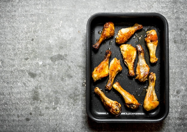 Pernas de frango frito na assadeira. Na mesa de pedra.