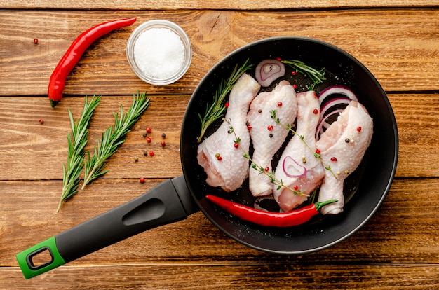 Pernas de frango marinado cru ou coxinhas de frango com temperos e ervas em uma frigideira pronta para cozinhar. conceito de comida mediterrânea. vista do topo