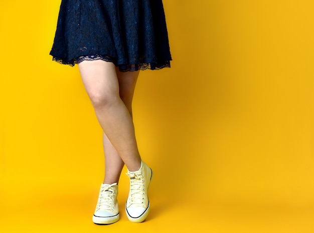 Pernas de garota usando vestido azul em fundo amarelo