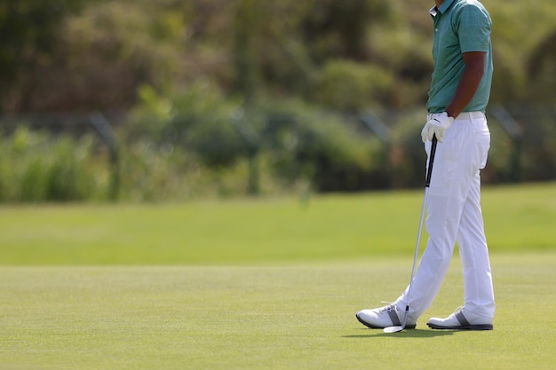 Pernas de jogador de golfe no buraco de bola de golfe golfista posando em campo verdejante