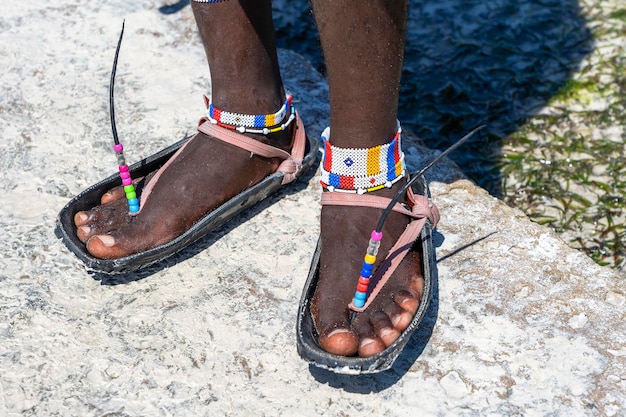 Pernas de masai tribais com uma pulseira colorida e sandálias feitas de pneus de carro fecham a ilha de Zanzibar Tanzânia África