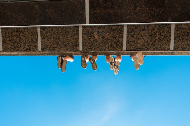 Pernas de meninos com sapatos pendurados na ponte contra o céu azul