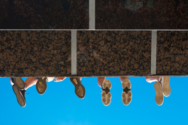 Pernas de meninos com sapatos pendurados na ponte contra o céu azul