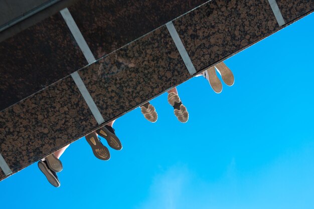 Pernas de meninos com sapatos pendurados na ponte contra o céu azul