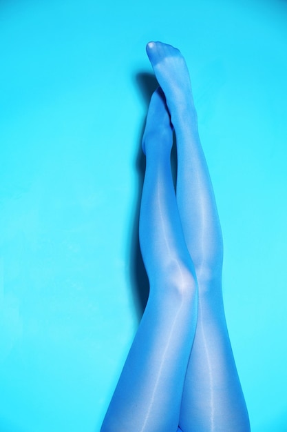 Pernas de mulher bonita em meia-calça de cor sobre fundo azul