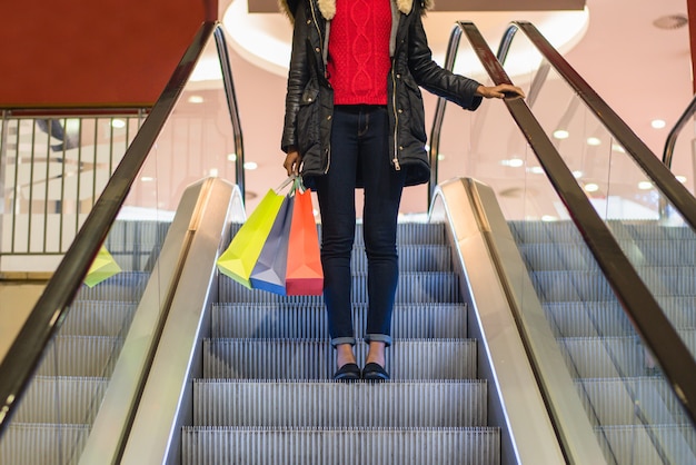 Pernas de mulher com sacolas coloridas na escada rolante em um shopping