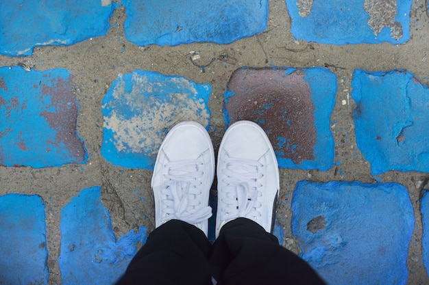 Pernas de mulher de tênis branco no vintage azul pintado pavers