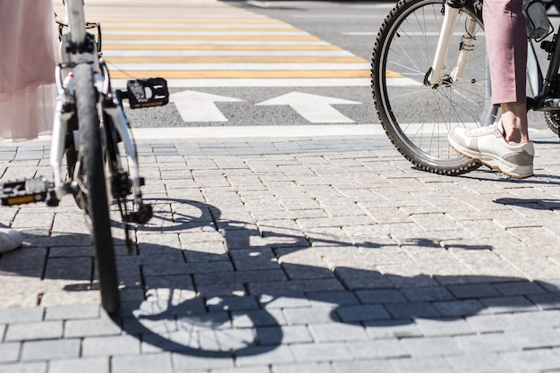 Pernas de mulher em pé perto de uma bicicleta e pernas de homem de bicicleta na calçada em frente ao cruzamento