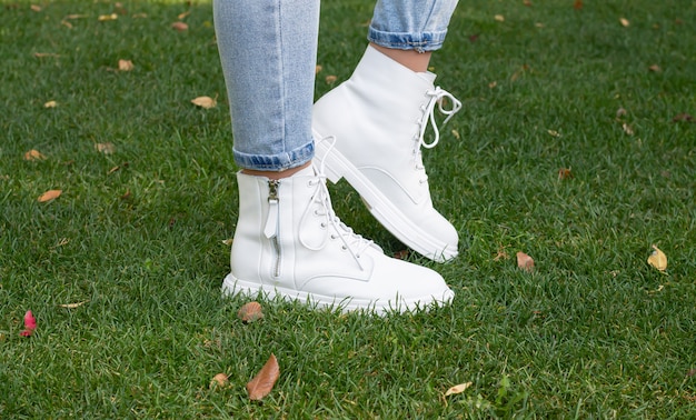 Pernas de mulher na moda botas casuais brancas na grama verde