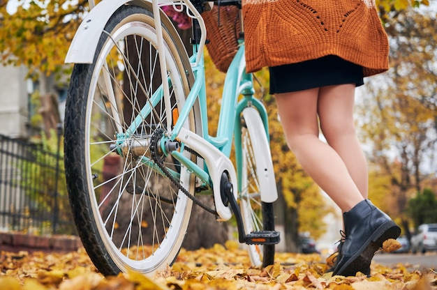 Pernas de mulher perto de bicicleta com cesta na rua outono