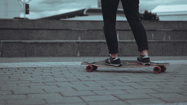 Pernas de mulher skatista andando de skate na cidade cinza